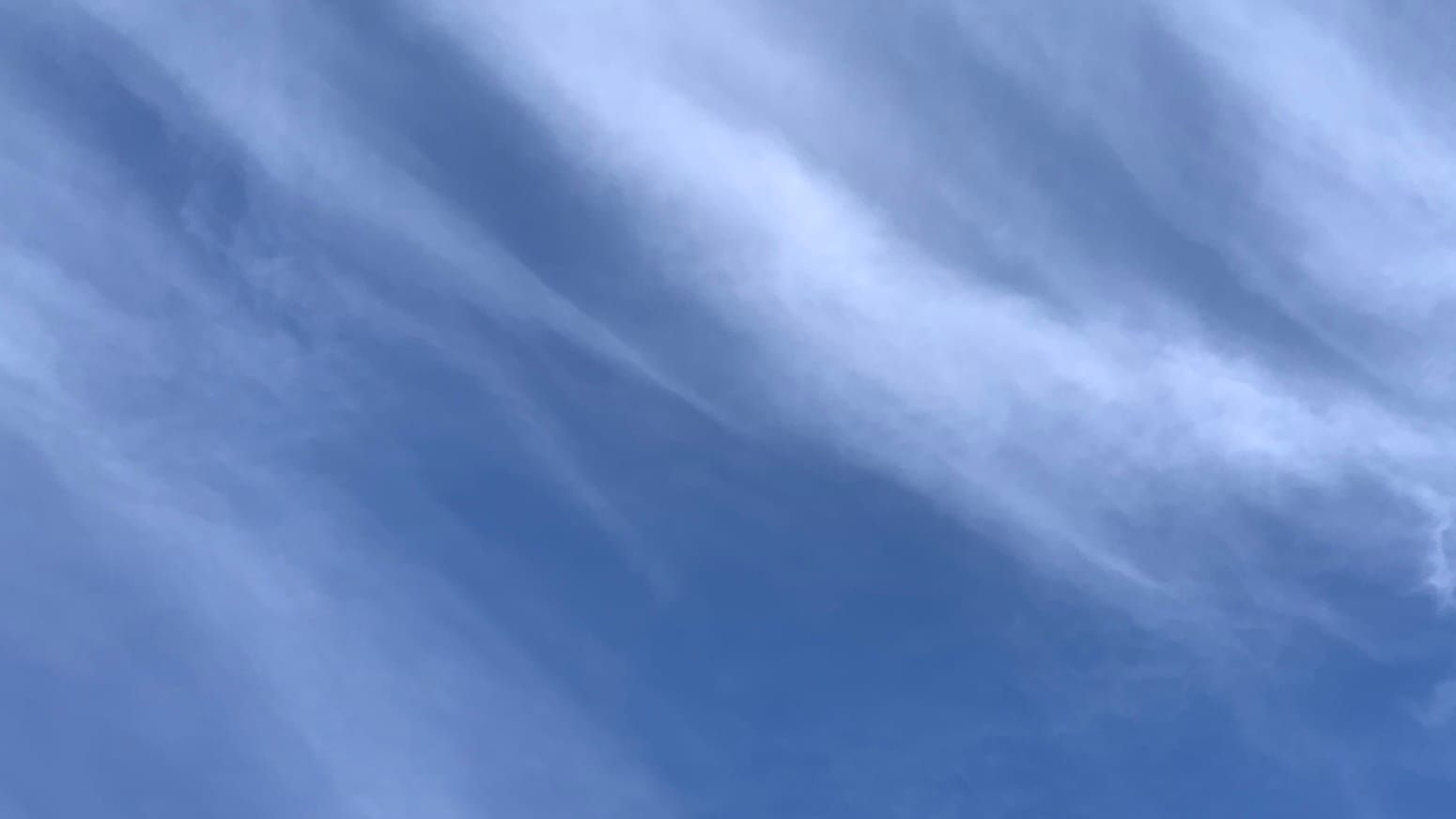 A patch of blue sky with wispy tapering streaks of cloud going diagonally across it from upper left toward lower right, creating a sort of loosely striped effect.