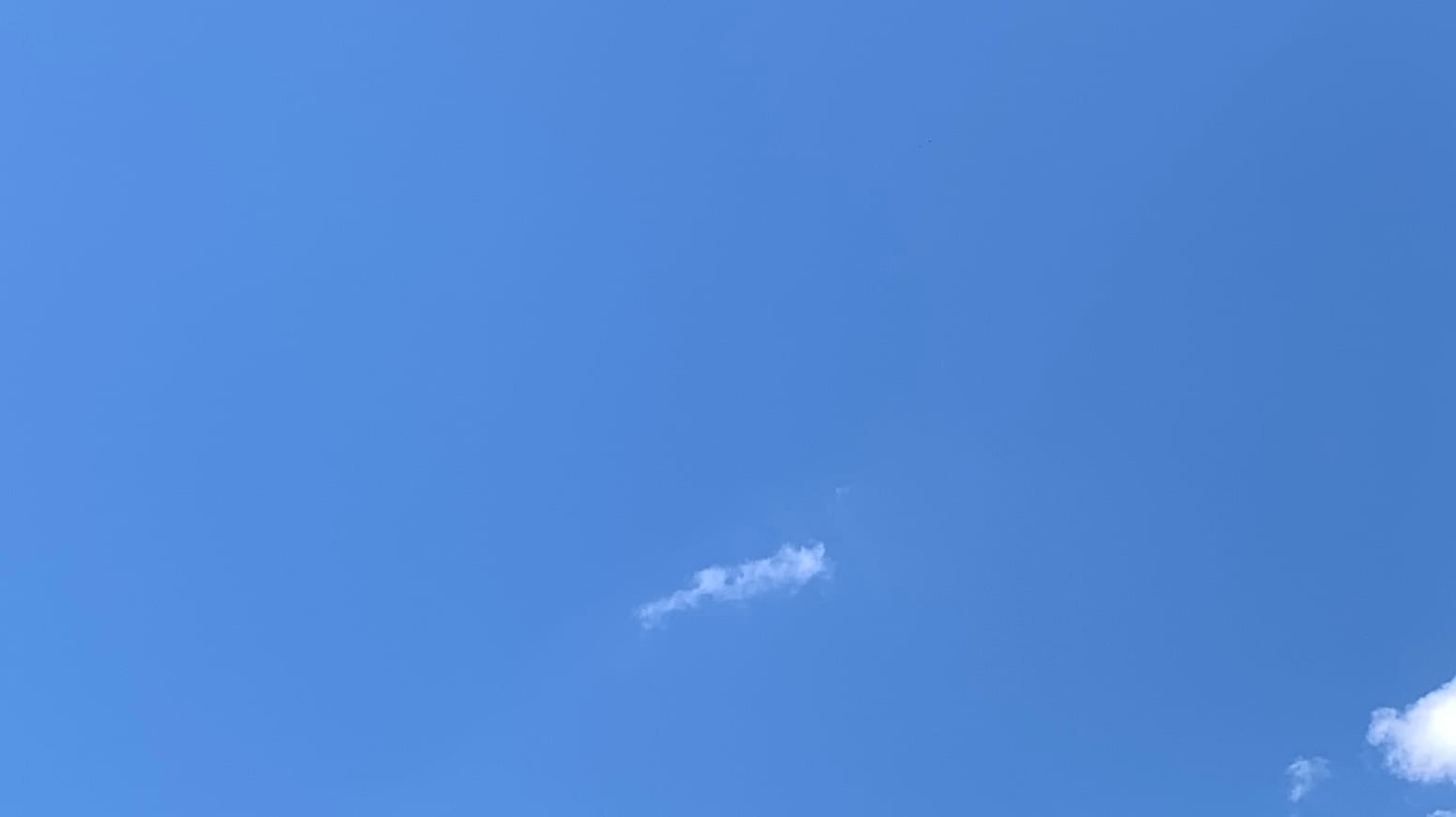 A patch of blue sky with a small cigar-shaped cloud, tipped slightly up from horizontal, in the lower middle of the frame, and a bit of a larger, brighter-white cloud poking in from the bottom of the right edge. 