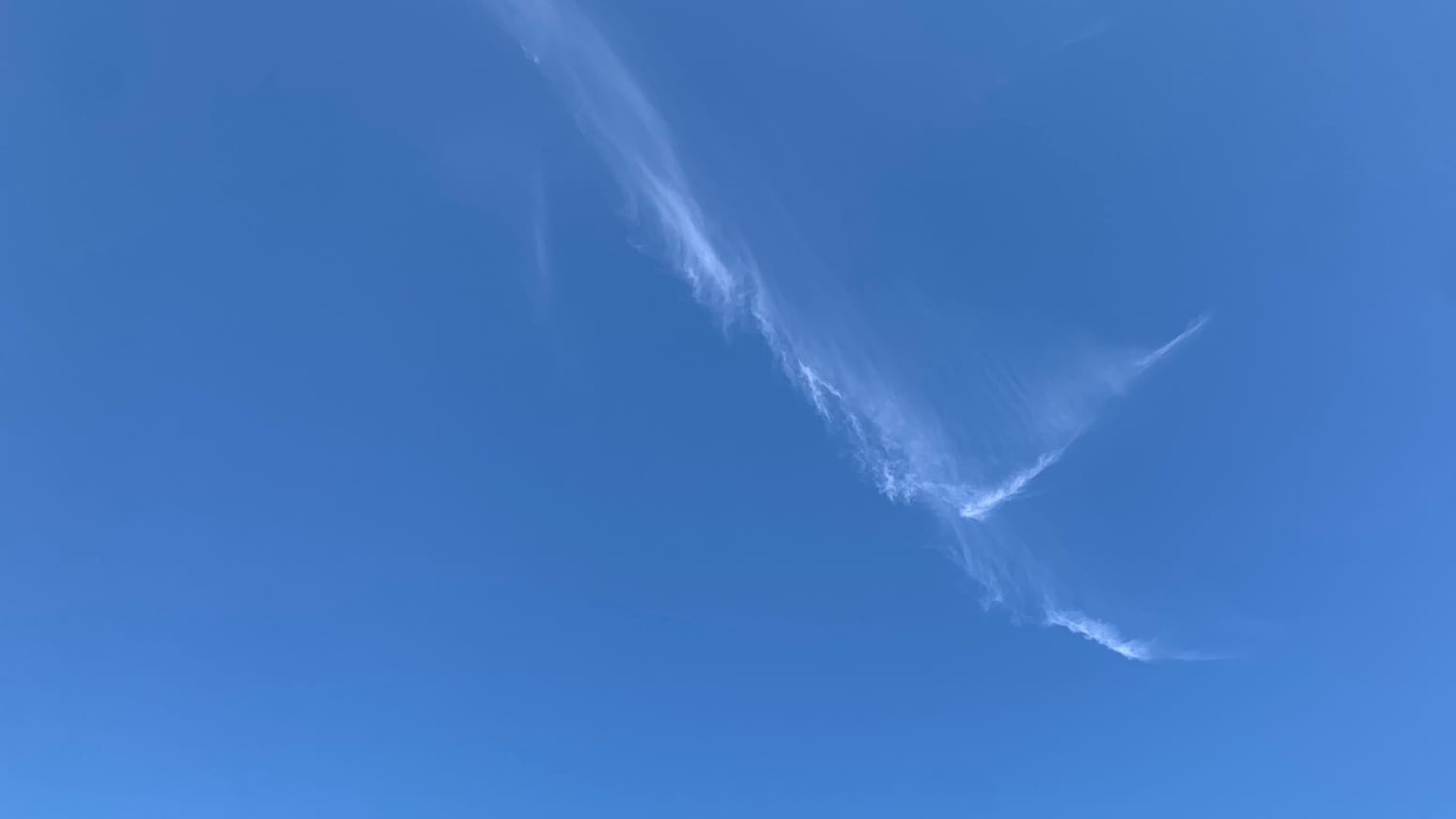 A patch of clear blue sky with a sharply forking arrangement of wispy line segments of cloud, like a sideways lowercase Y, entering the frame near the top middle and angling toward the bottom right. 