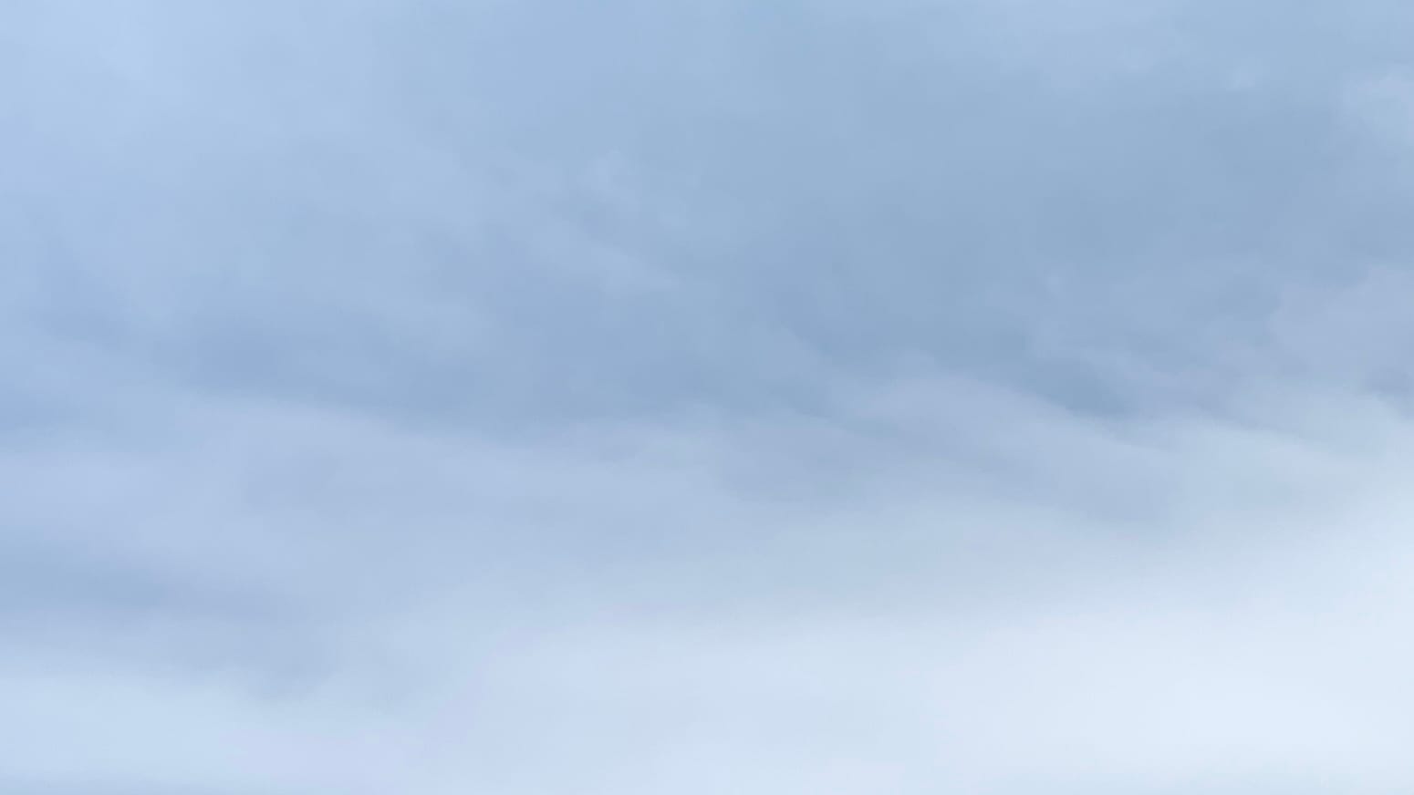 A patch of bluish sky overlaid with thin white cloud, with a sort of diagonal grain to it and thicker toward the bottom of the frame. 
