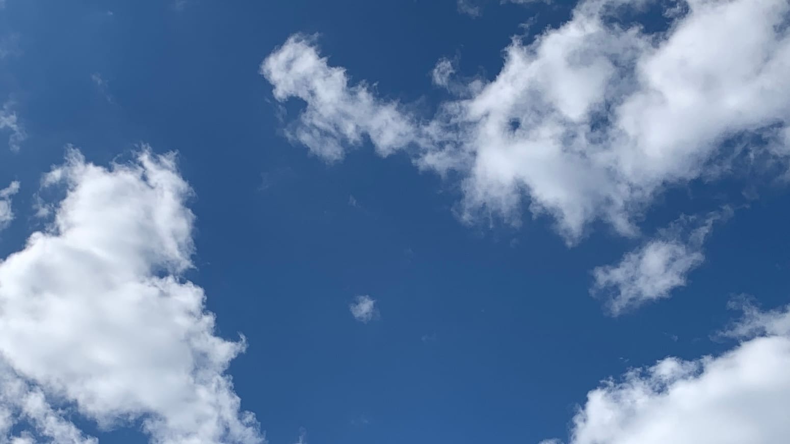 A patch of deep blue sky with loose bright white clouds poking into it from three of the corners of the frame, all but the top left. 