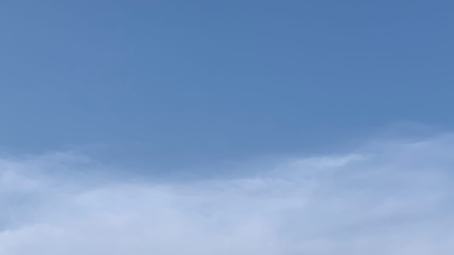 A patch of sky, divided between a top two-thirds or so of blue and a bottom one-third or so of translucent white. There are overlapping undulations along the boundary between the two, so the division is definite but not entirely distinct. 