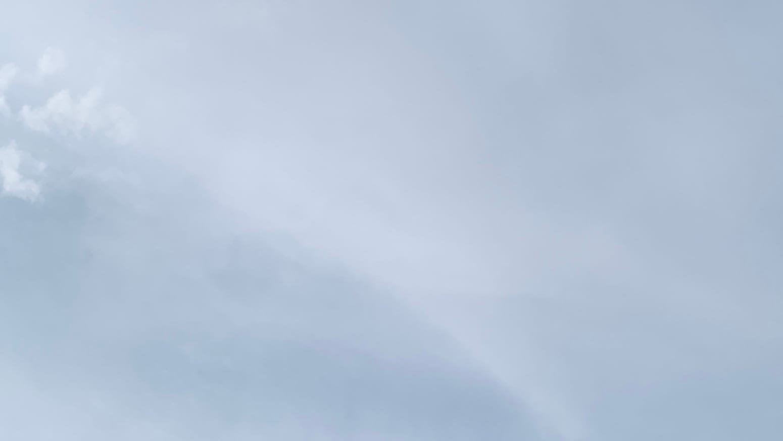 A patch of gray sky with an indistinct lighter gray streak curving from upper left to the right side of the bottom of the frame, and with some tiny scribbled-looking little puffs of even lighter gray peeping into the upper part of the left side. 