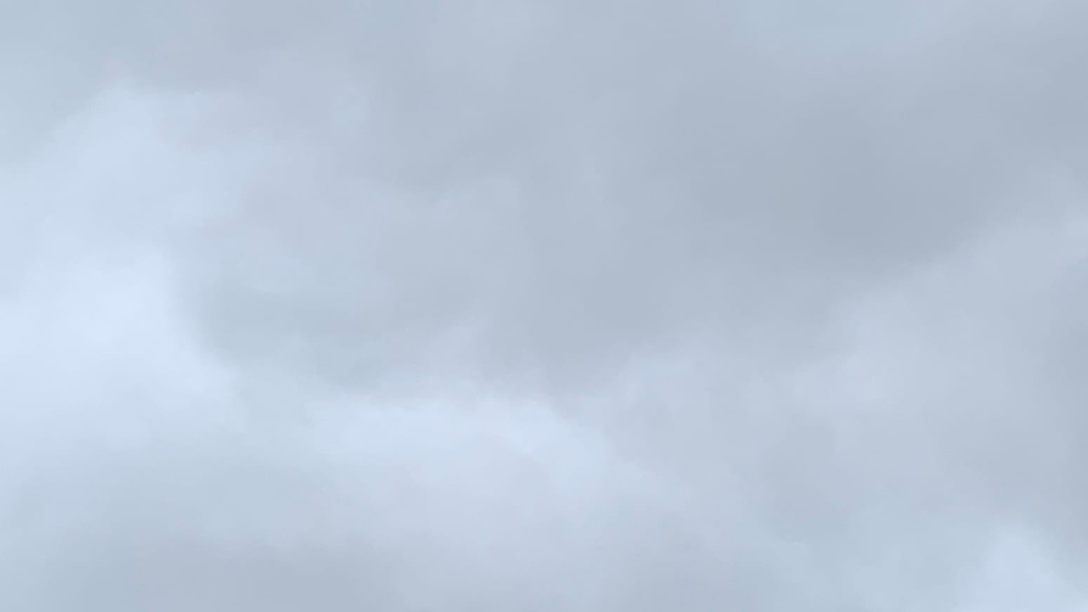 A patch of cloudy gray sky with an irregular and weakly defined seam running along the middle between slightly darker gray clouds above and slightly lighter ones below. 