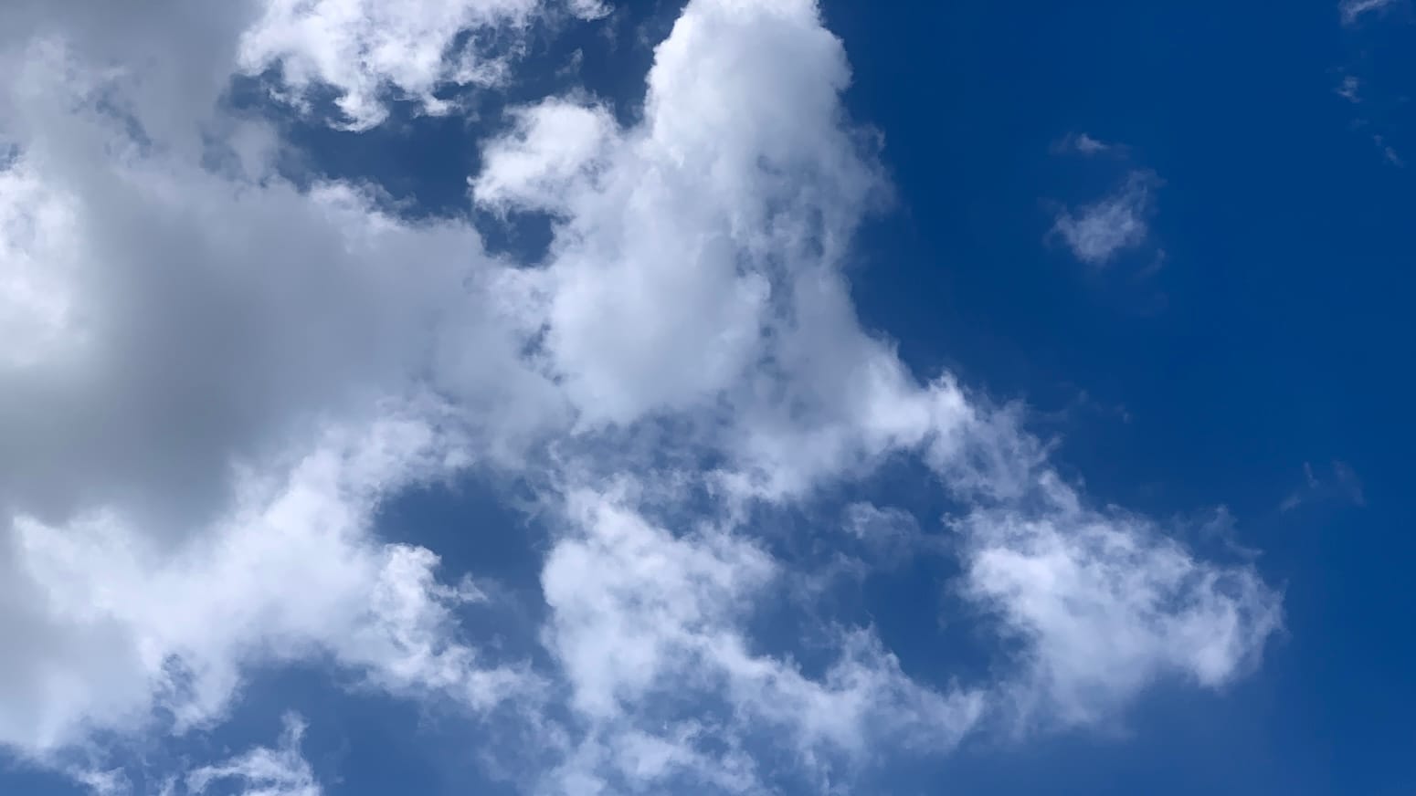 A patch of deep blue sky with broken white clouds overlaid on the left and middle of the frame. To the far left some parts of the clouds are a smooth gray. 
