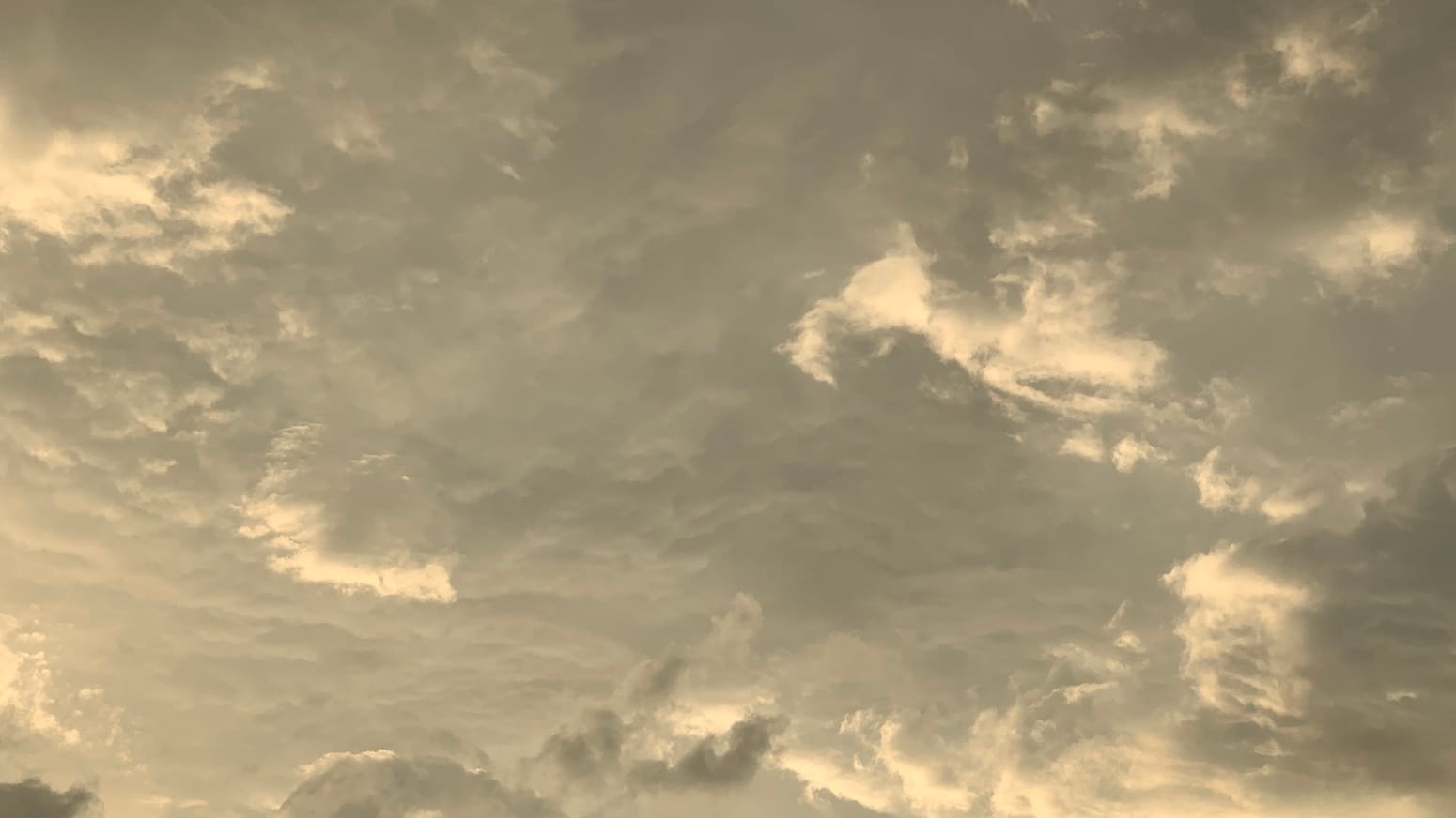 A churned-up sky of yellow-tinted silver, lit from below, with a few dark scraps of cloud at the bottom left, overlaid on the other cloud. 