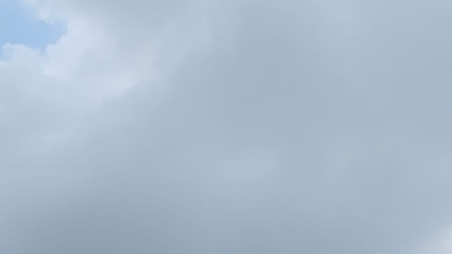 A patch of sky almost entirely filled with medium gray cloud, opening to admit a little hooked patch of dusty blue sky in the top left corner. 