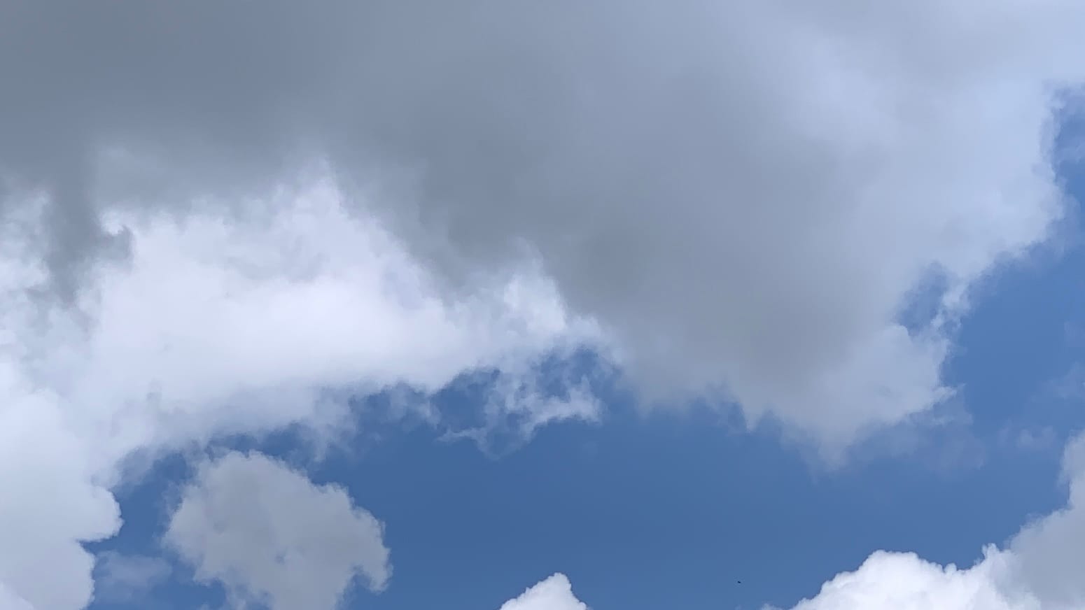 A patch of sky with smooth-looking gray cloud dangling from the top of the frame. Below and behind the gray is white cloud parted to allow an arm of deepish blue to run across the lower part of the frame. A single puff of the same gray as the upper part is framed inside the tip of the blue region. 