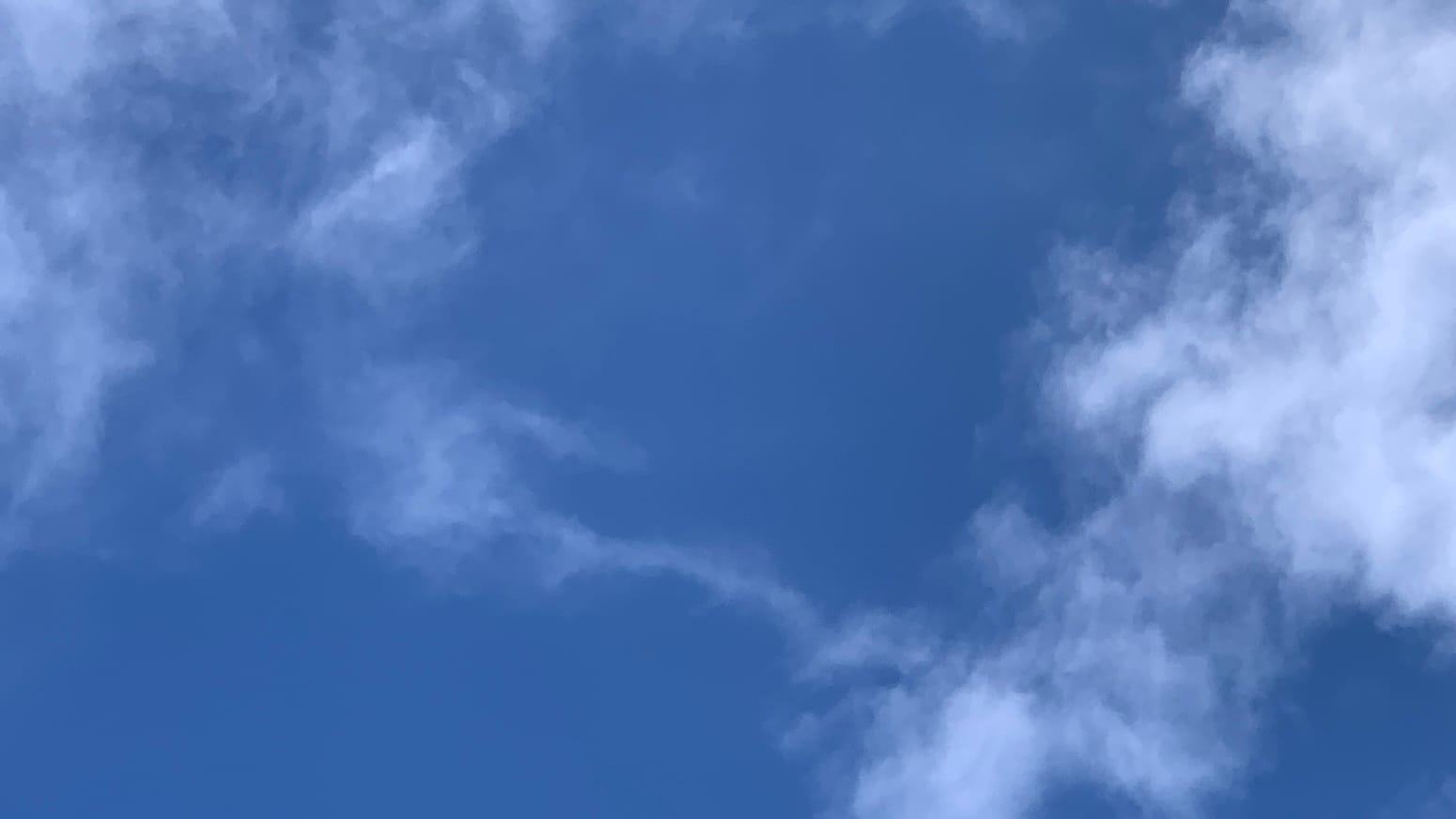 On a deep blue patch of sky, two bits of loose white cloud are connected by a very narrow cloud-isthmus. 