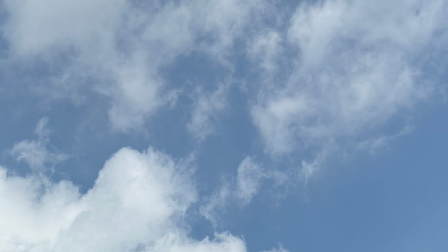 A patch of sky with loose white clouds reaching in from above and below against a background of haze-dusty blue. 