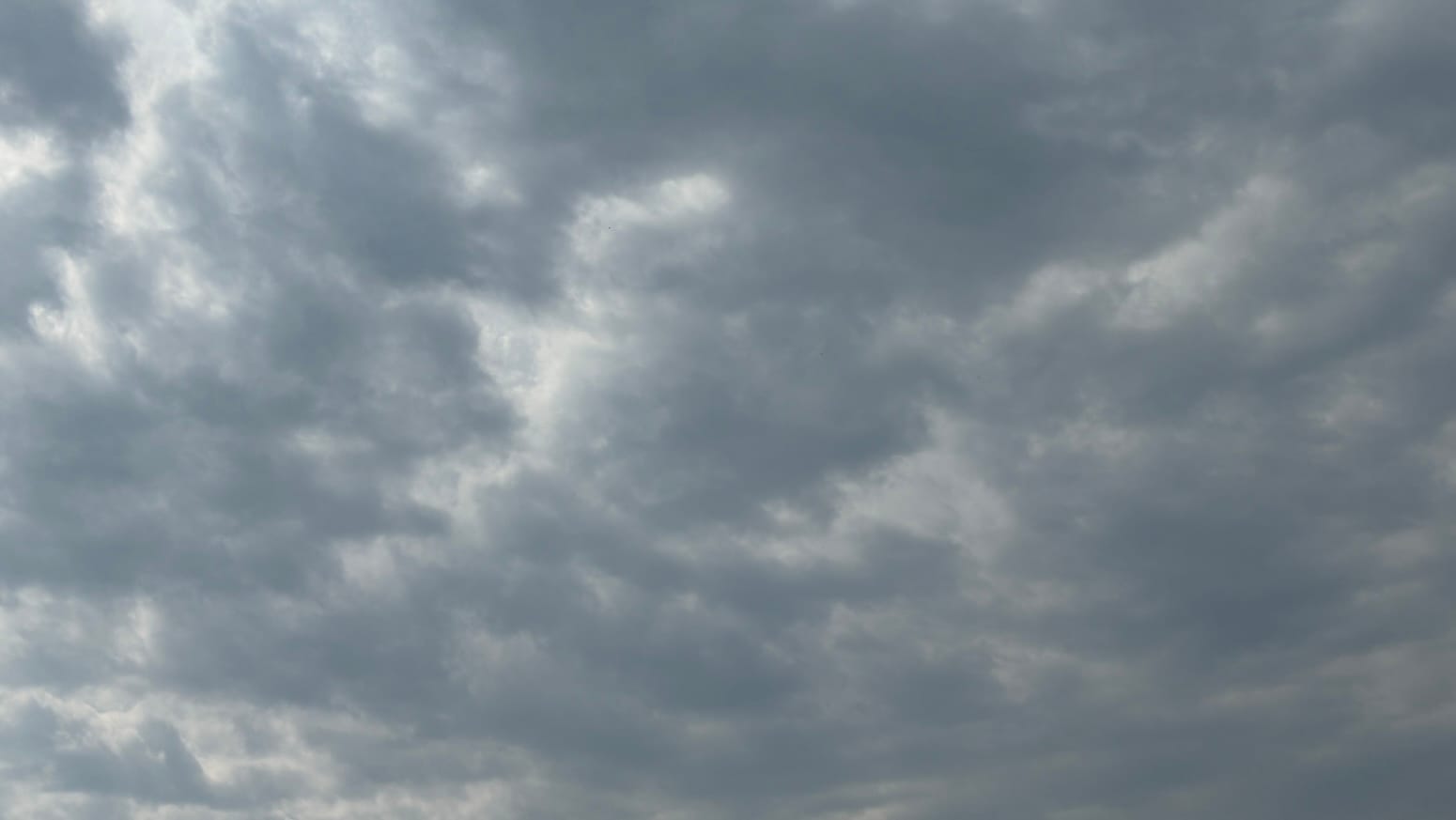 A patch of sky filled with clumped-together gray clouds with brighter parts where they meet. 