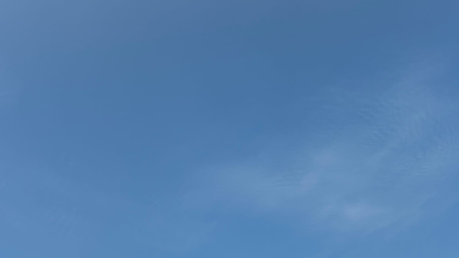 A patch of almost clear blue sky with a near-invisible, slightly ruffled patch of cloud toward the lower right part of the frame. 