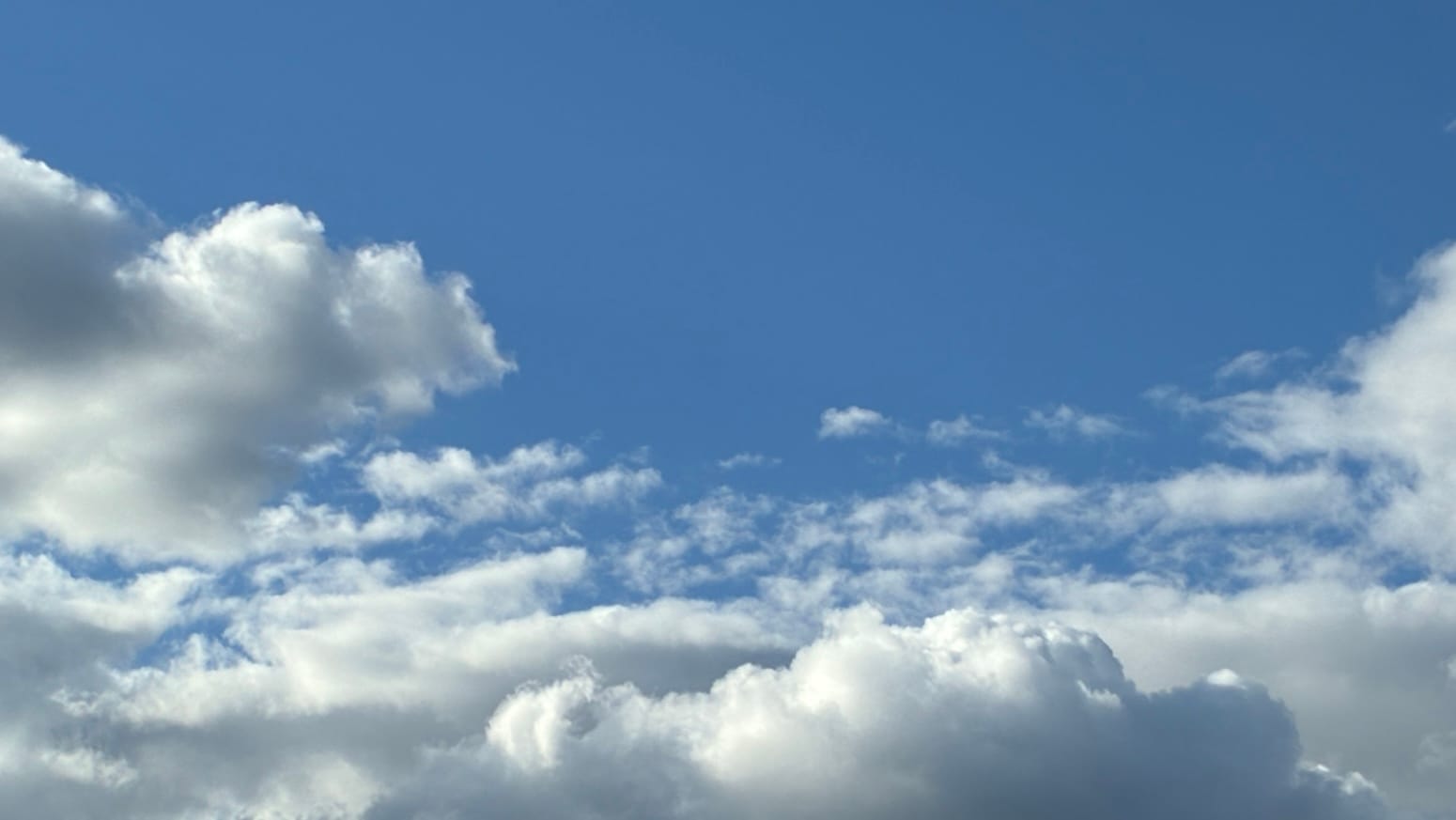 Ranks of different clouds, from loose small ones in the distance to a well-formed and three-dimensionally shaded one in the foreground, march in ranks toward the bottom edge of the frame. Above them all is an open expanse of deep clear blue. 