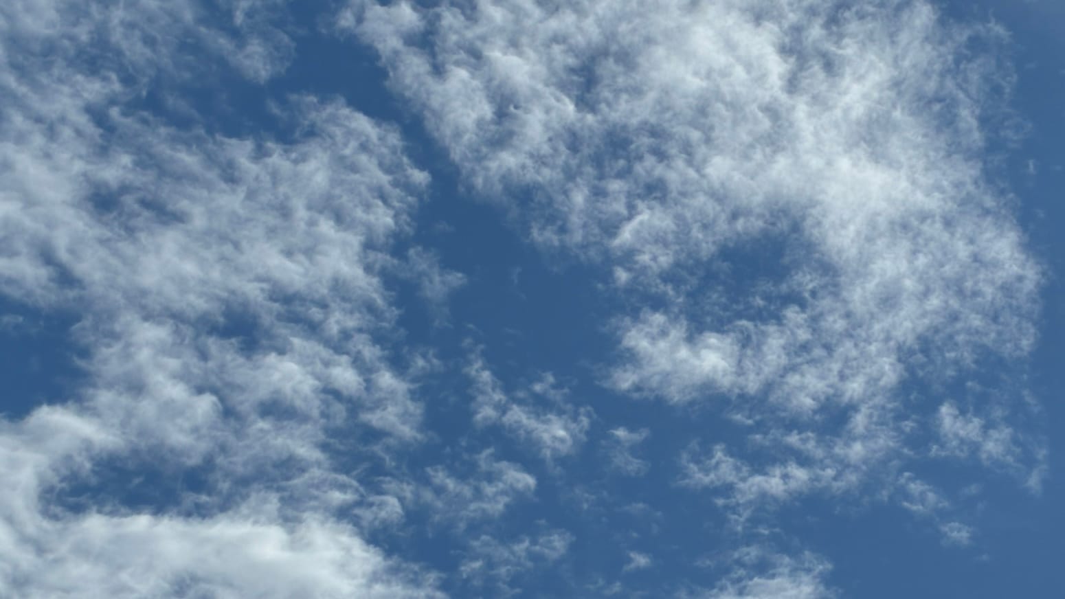A patch of deep blue sky with translucent patches of cloud on it, made up of choppy little white cloudlets like piled-up loose bits of punctuation. 