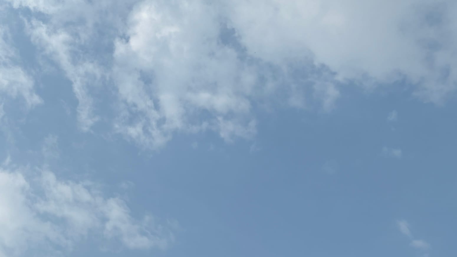 A patch of hazy, desaturated-blue sky with loose, haze-grayed clouds across the top of the frame and sticking into the lower left corner.