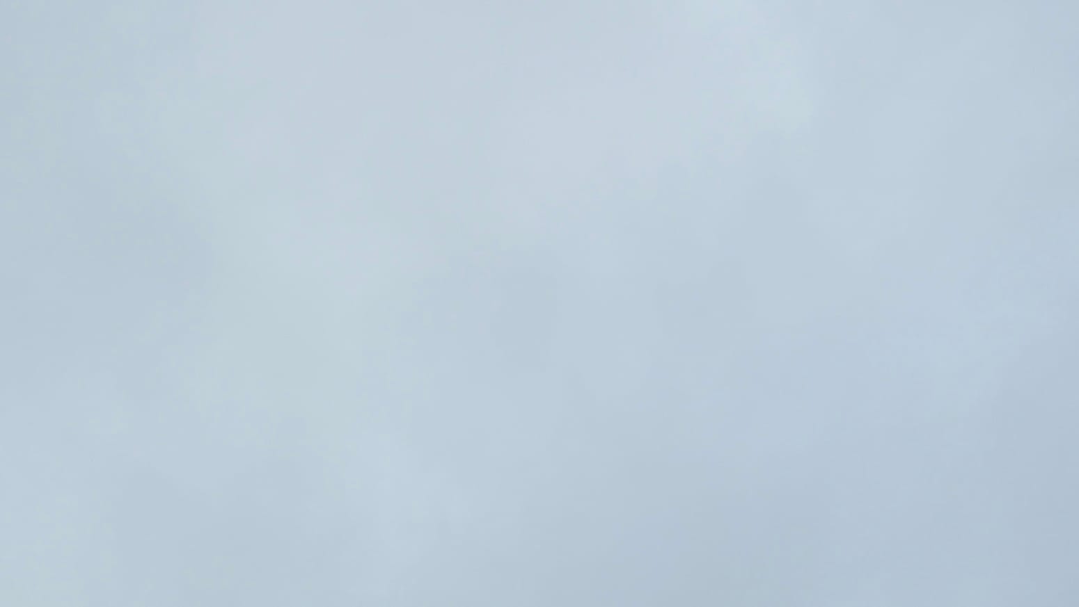 A patch of sky filled with an almost even-toned sheet of medium-light gray cloud.