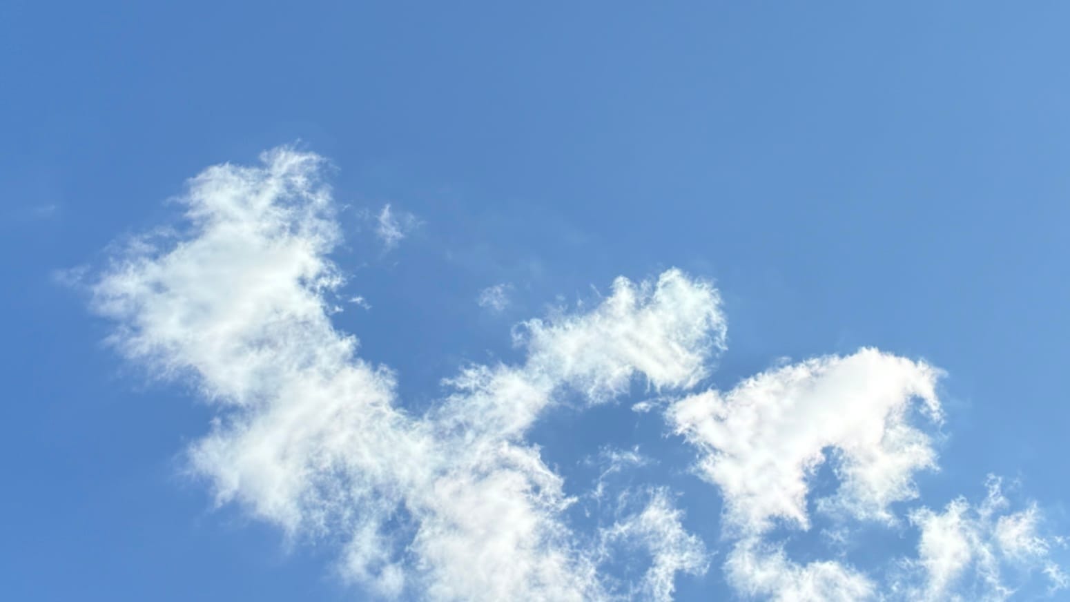 A patch of blue sky with loose white clouds in the middle and bottom of the frame.