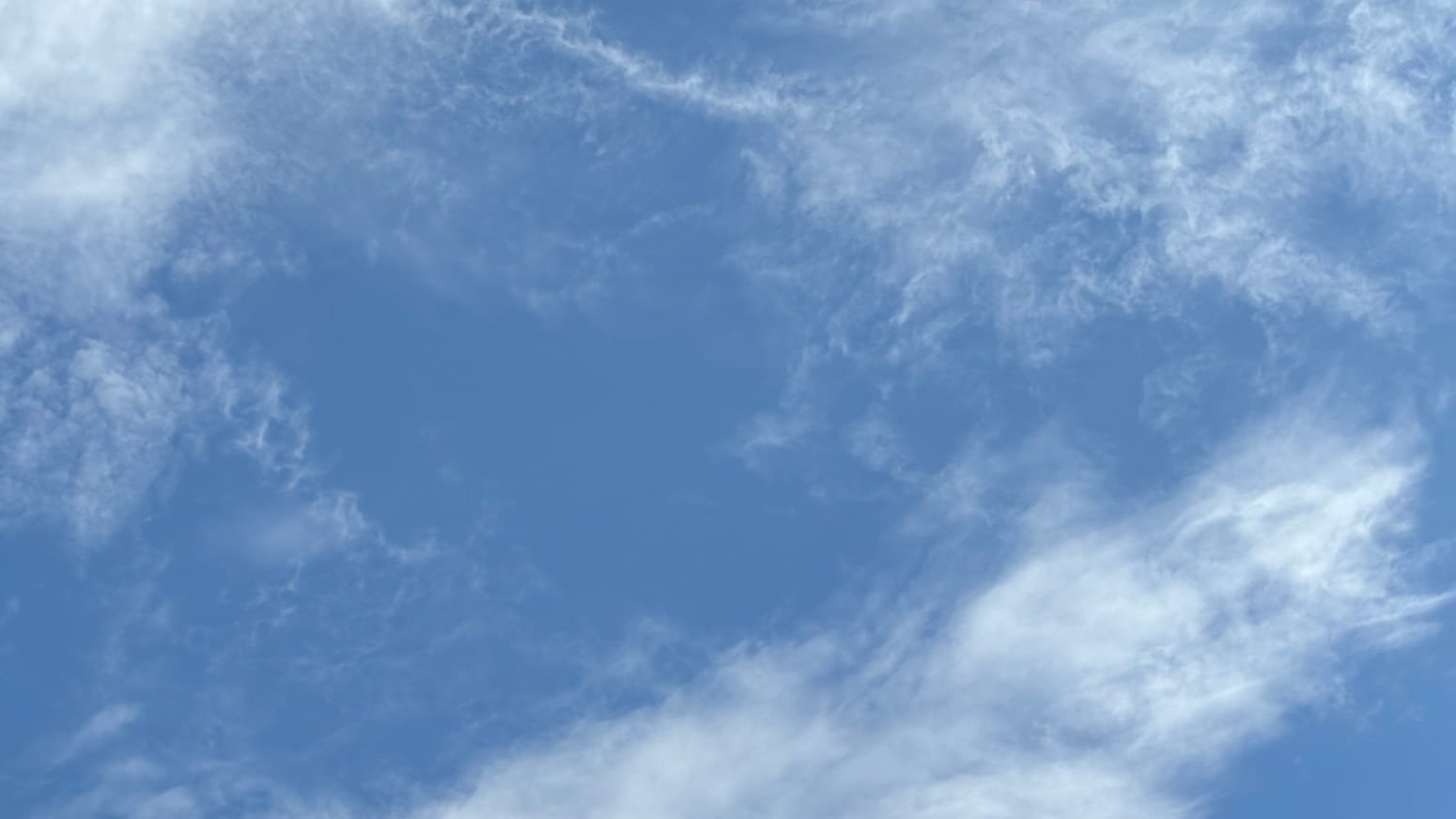 A patch of blue sky overlaid with translucent white clouds along the top and across the bottom right corner of the frame.