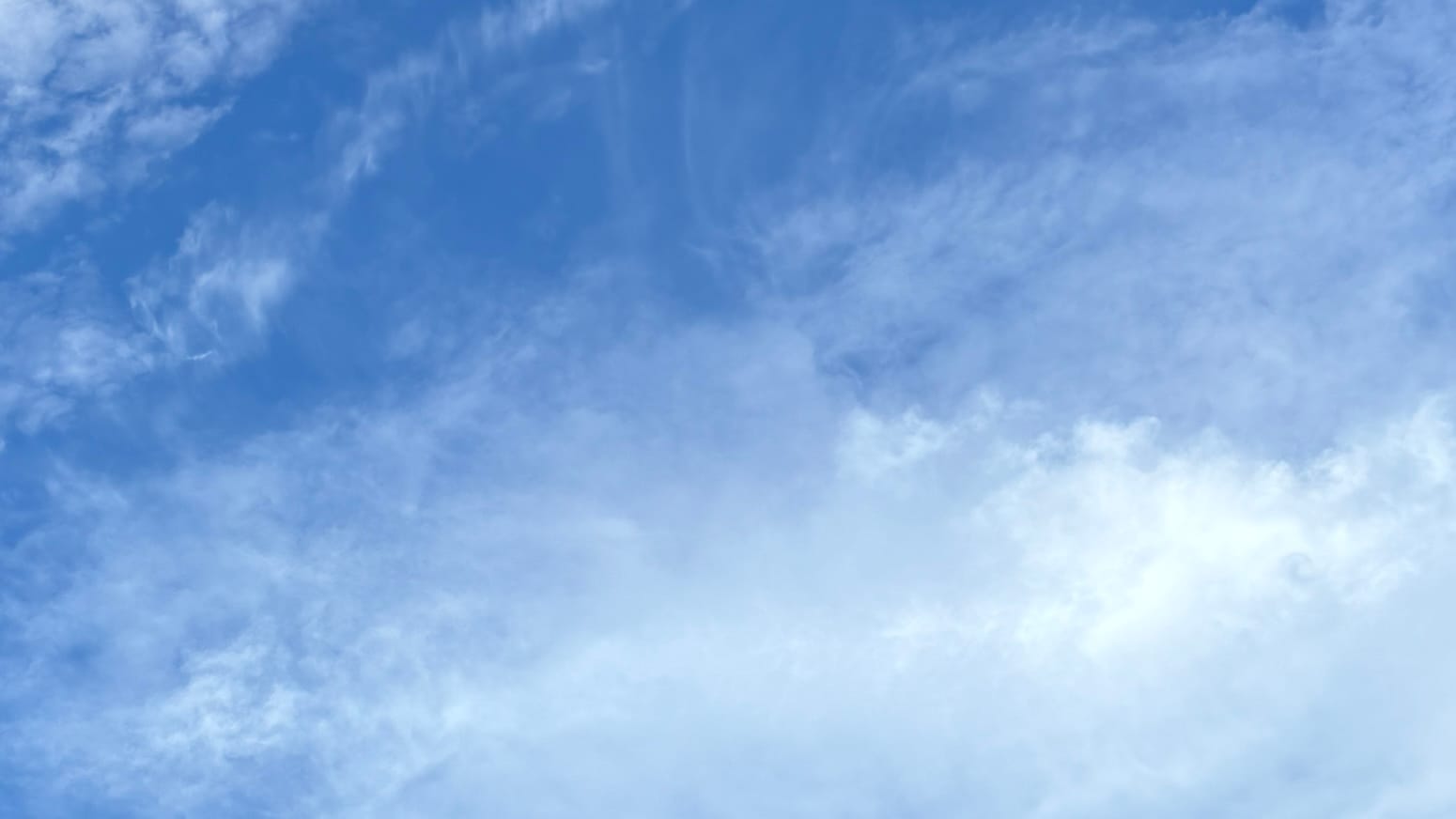 A patch of brilliant lapis lazuli sky, overlaid, especially in the middle and bottom of the frame, with uneven transparent white cloud. One portion of the cloud, toward the mid-lower right, is more densely clumped and brilliant pure white.