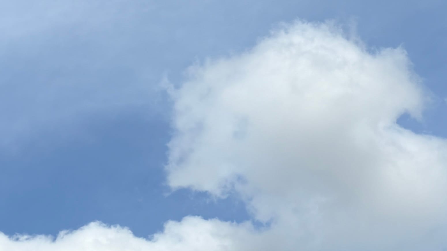 A patch of medium blue sky, with transparent white cloud overlaid on it toward the top of the frame and a line of solid white cumulus running along the bottom, with a swelling dome of the cumulus rising from that to take up most of the right-hand part of the frame. The whole thing looks like part of the sky in a painting on the cover of a Del Rey fantasy paperback.