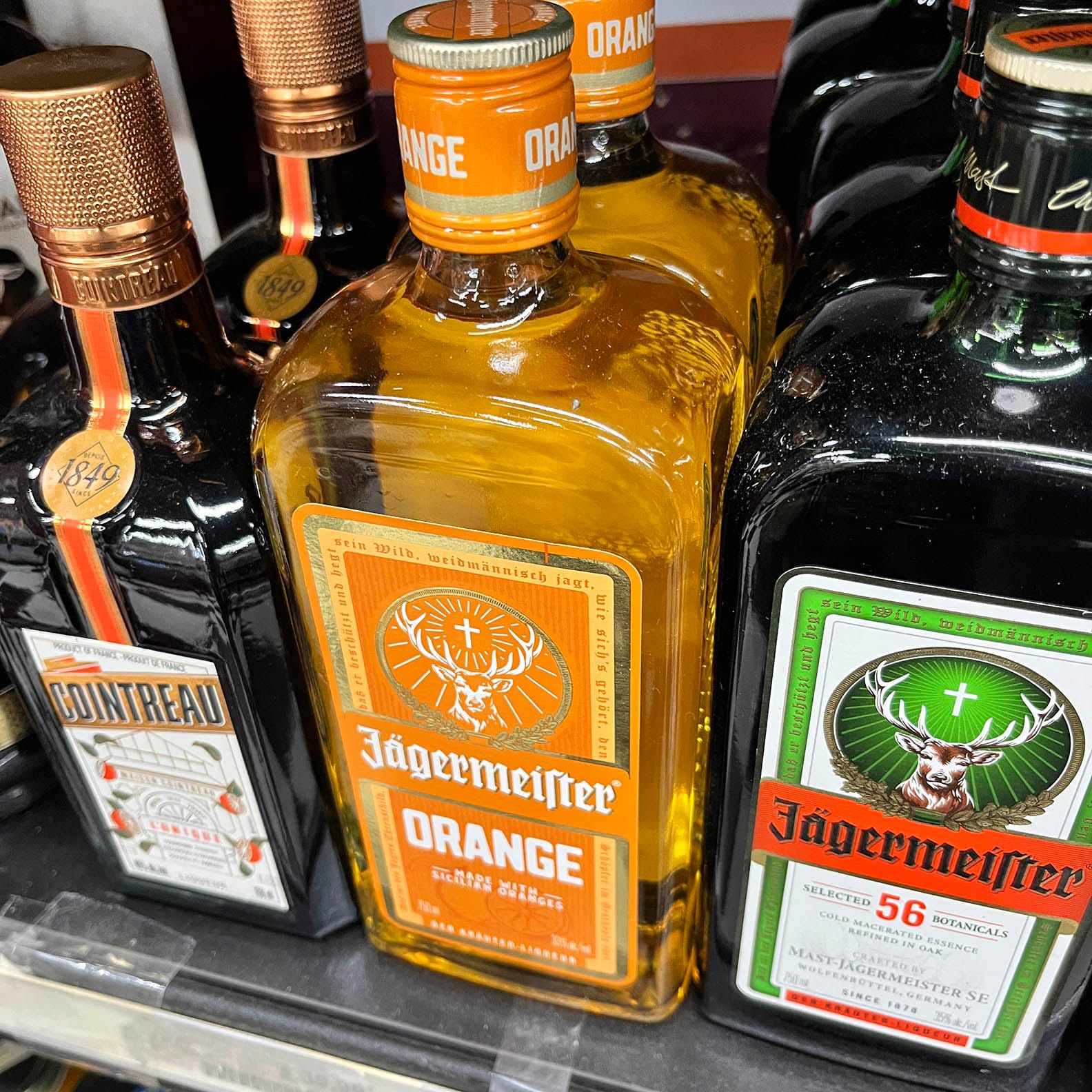 On a shelf at the liquor store: JÄGERMEISTER ORANGE between regular Jäger and COINTREAU