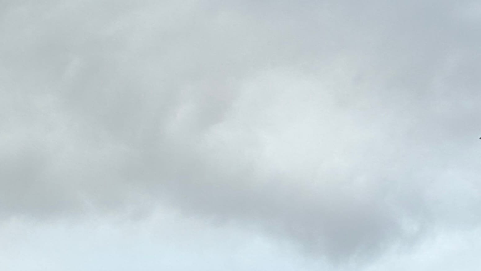A patch of sky with medium-light gray clouds hanging down to brush the bottom of the frame, where there's otherwise a patch of a more bluish gray or a gray thin enough to let some blue show through..