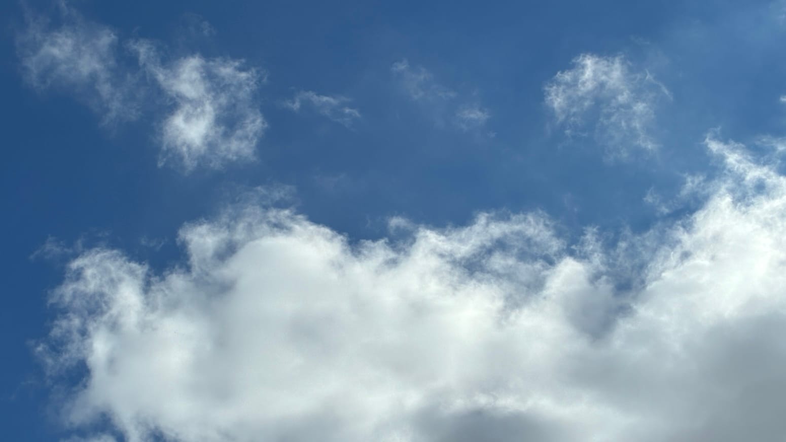 Alt: A patch of deep blue sky with a loose-edged, vaguely peanut-shaped white cloud running along the bottom and little white scraps of cloud above.