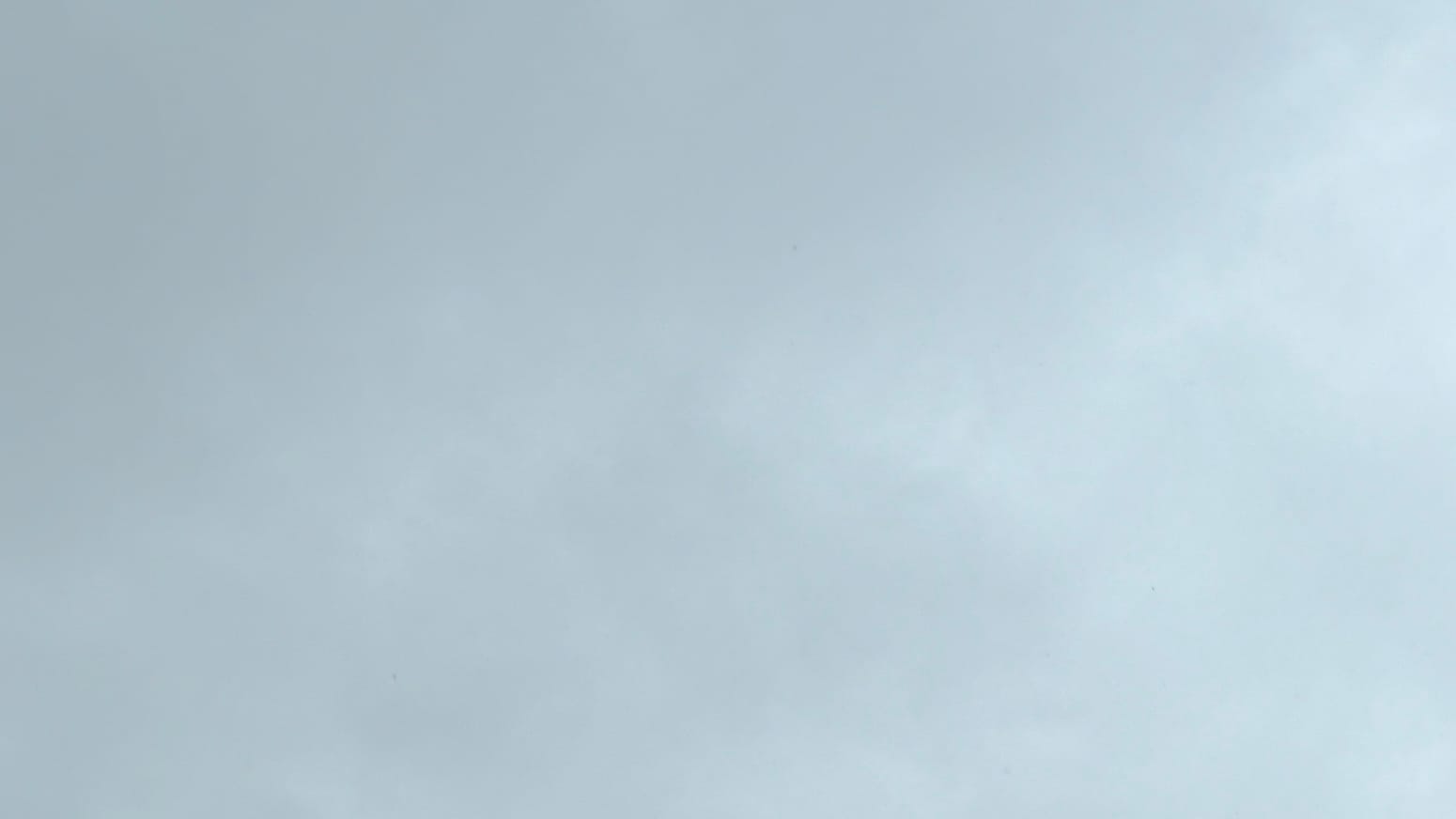 A patch of cloudy sky in an uneven medium gray, with more lighter parts toward the right side of the frame