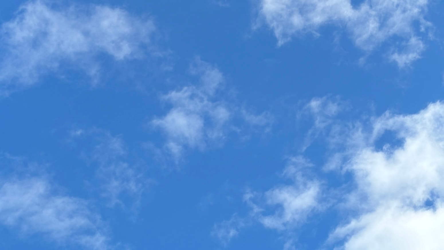 A patch of more or less azure blue sky with smallish, loosely formed, translucent white clouds scattered across it.