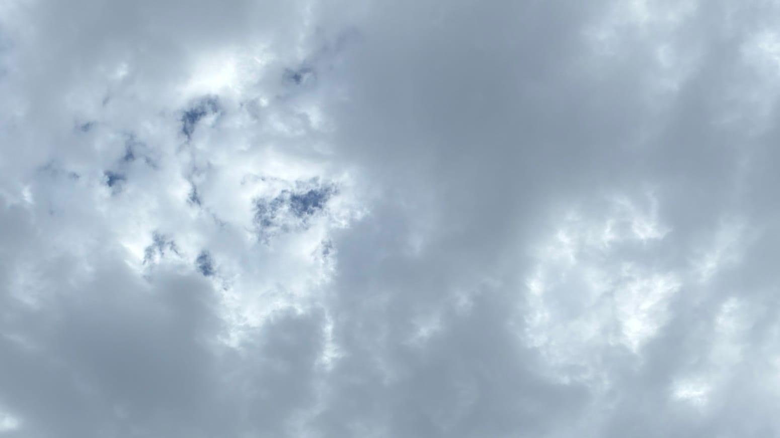 A patch of sky with agitated-looking dark gray clouds dimpled with bright spots. Some of the spots toward the upper left are hanging open to reveal little spots of deep blue sky behind them. 