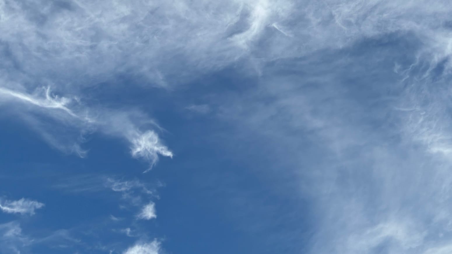 A patch of deep blue sky overlaid with white cloud in translucent patches and bright little snips, spreading and twisting every which way at once. The bottom left part of the frame has more open blue than the rest but also has three of the most concentratedly white little bits of cloud