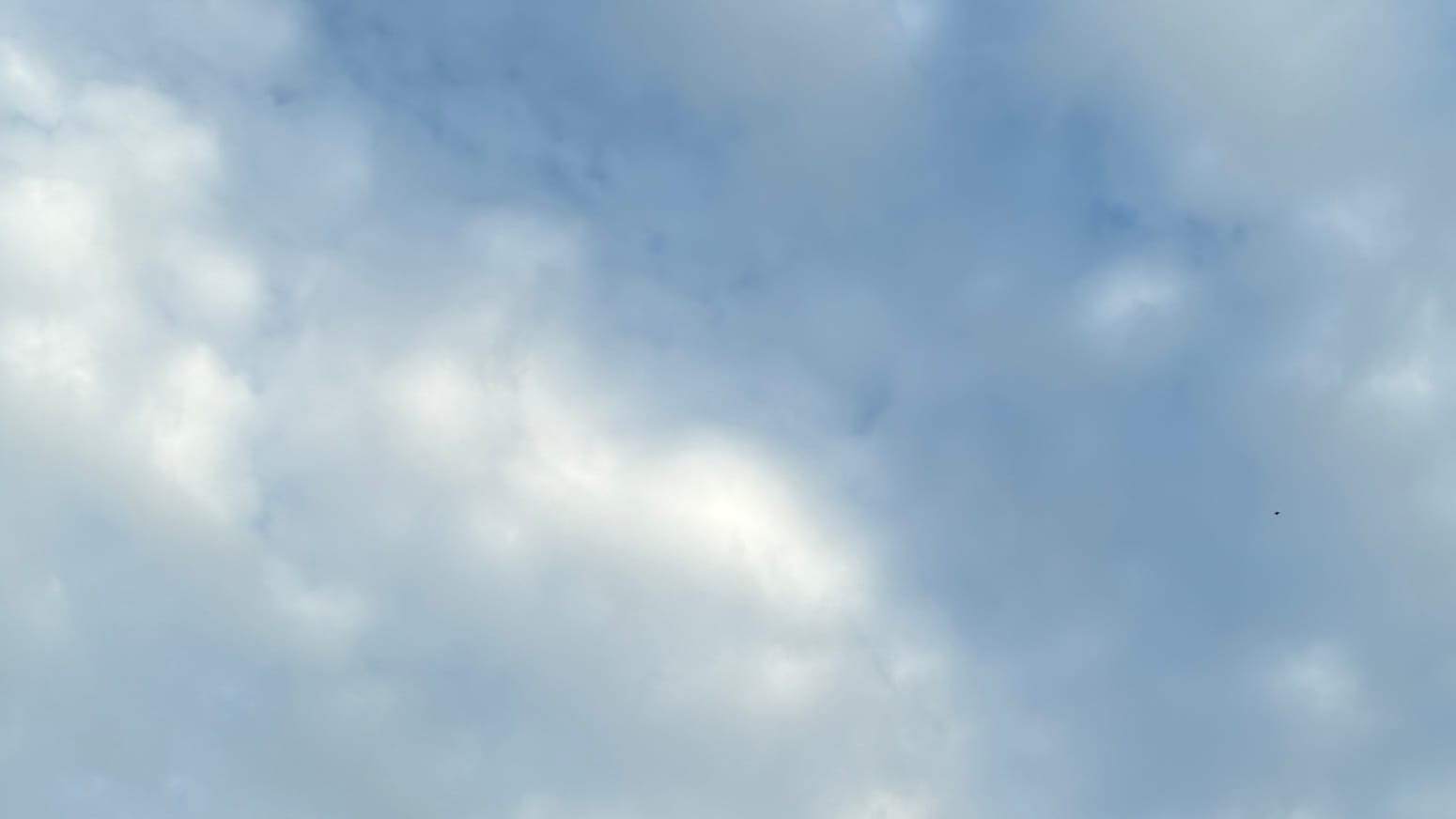 A patch of sky divided roughly along a top-left to bottom-right diagonal between gray cloud cover mottled with brilliant white, and translucent cloud cover mottled with gray, with blue showing through the thin parts.