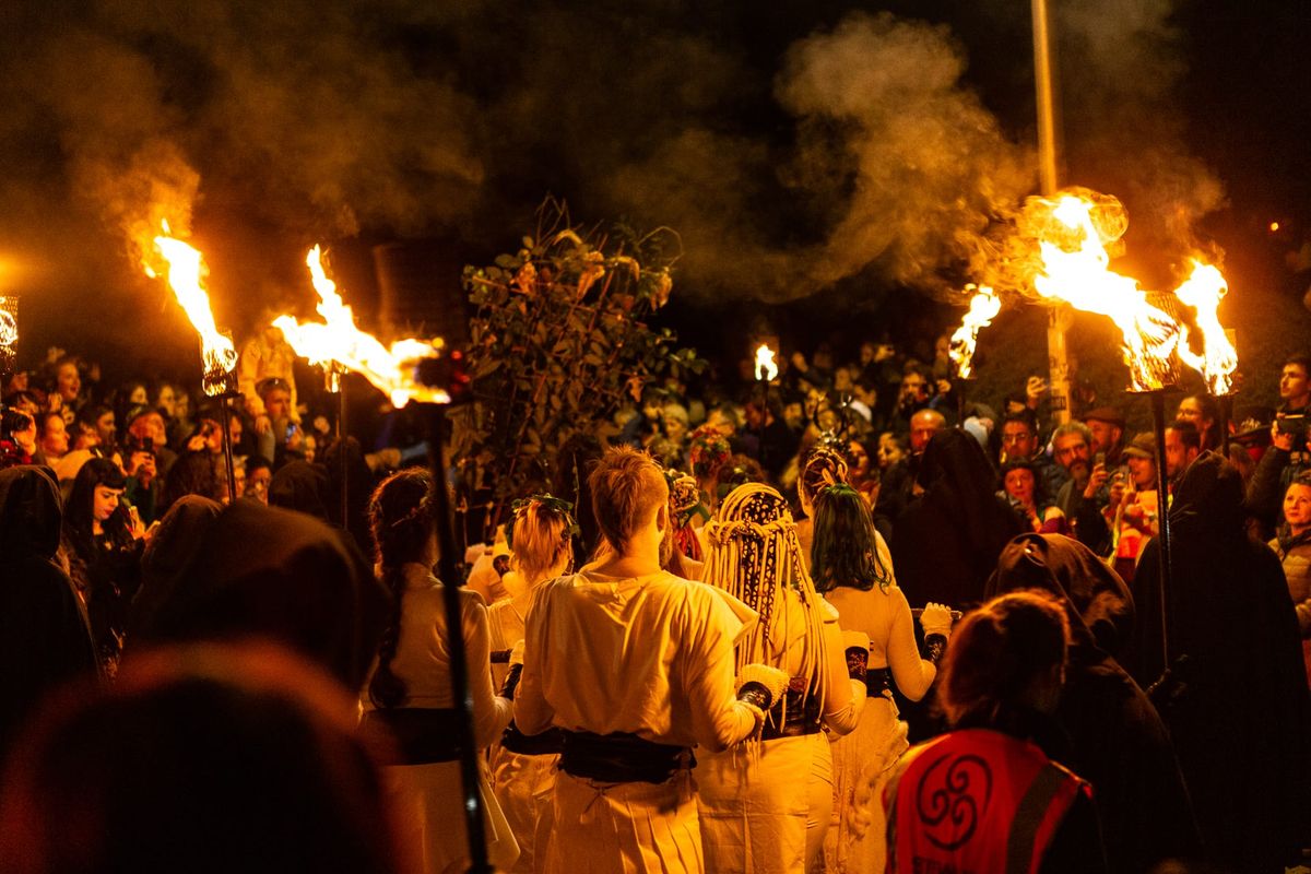 A night scene with people in ye old-looking garb and there's flower arrangements a pole and torches