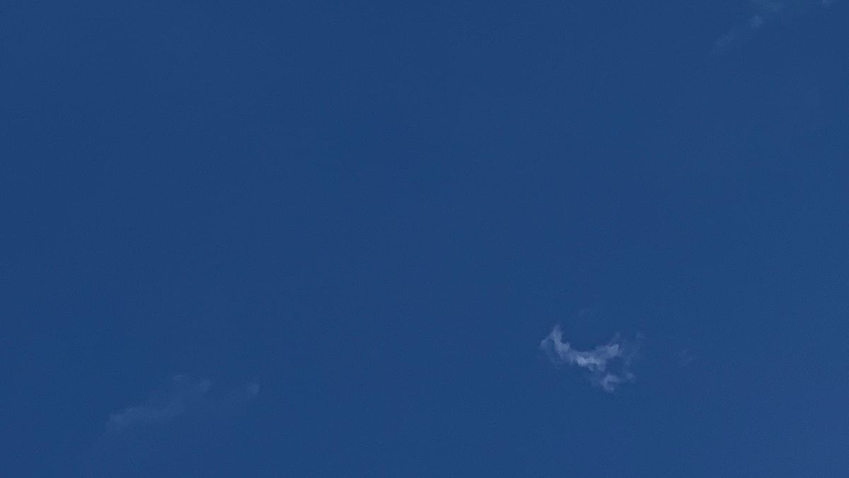 A blue sky with two small shreds of cloud floating in it, one almost invisible