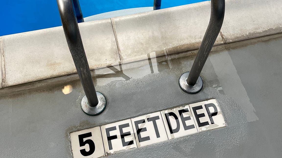 Depth marker signage in tile in the floor near a ladder to a hotel pool. 5 FE ET DE EP.