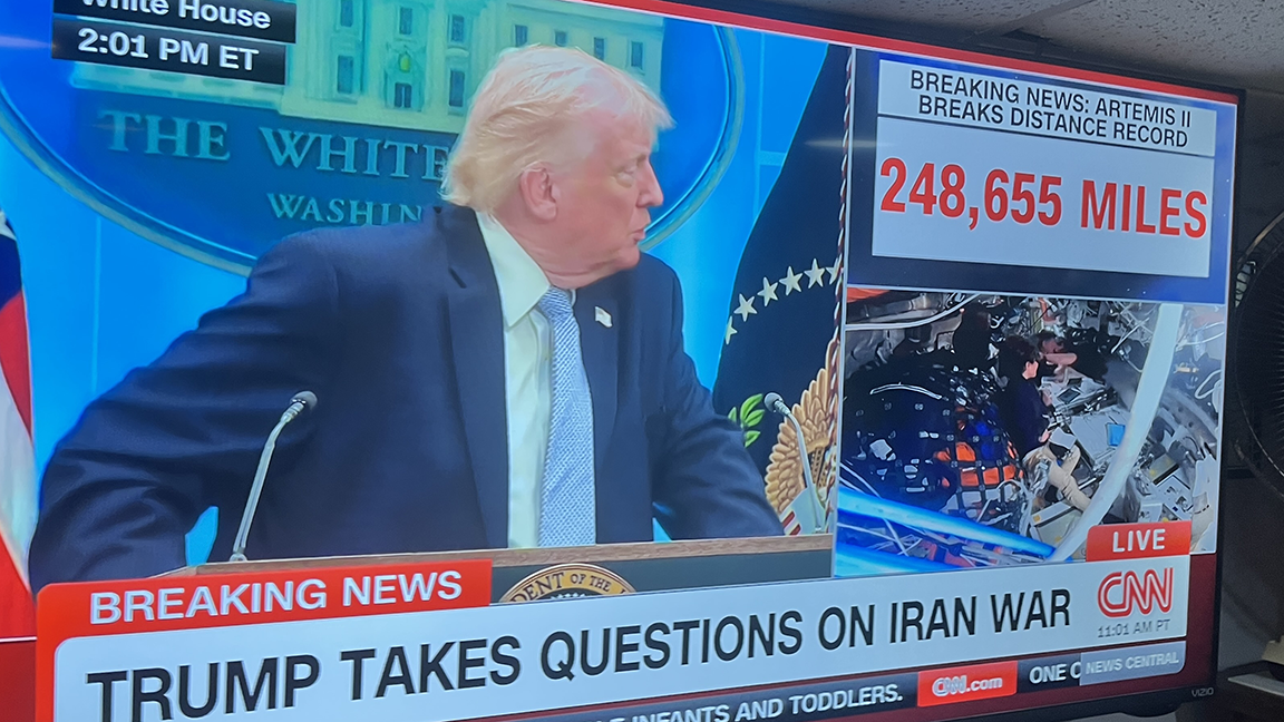 TV screen running CNN Trump press conference and ARTEMIS II moon shot. BREAKING NEWS: ARTEMIS II BREAKS DISTANCE RECORD 248,655 MILES BREAKING NEWS TRUMP TAKES QUESTIONS ON IRAN WAR