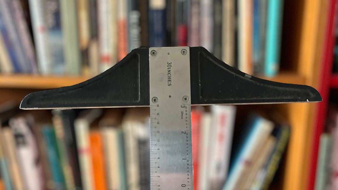 The top of a metal t-square with bookshelves in the background.