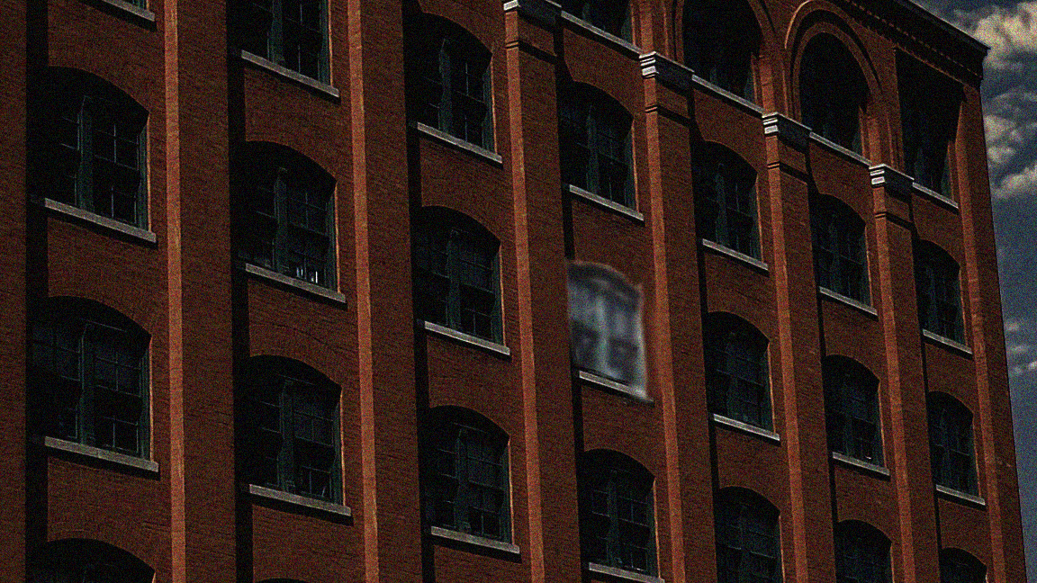 Exterior of a dark building with one window oddly highlighted.