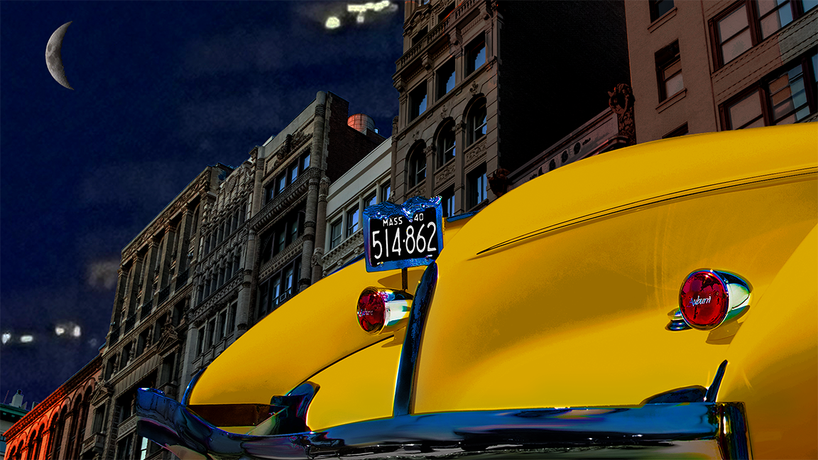 Rear of a yellow Auburn Boat Tail Speedster against dark buildings and a night sky with crescent moon
