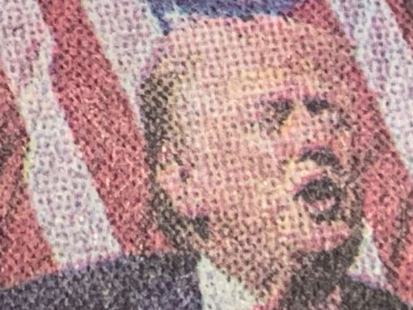 Deatil of New York Times photo of Donald Trump in front of an American flag making that mouth shape he makes.