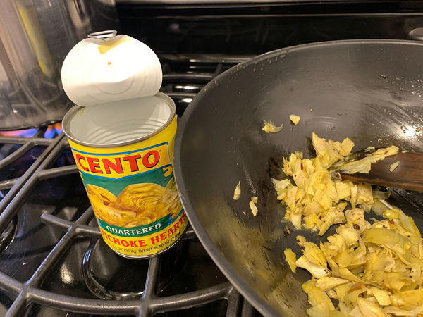 CENTO artichoke hearts can on gas stovetop with contents being stirred in wok