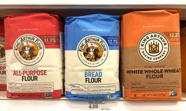 Three sacks of King Arthur flour, ALL-PURPOSE, UNBLEACHED BREAD, and WHITE WHOLE WHEAT, on a grocery shelf.