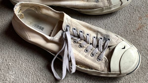 A flat battered sneaker with blown-out heel, holes in the toe shell and canvas ripping away from the rubber sides