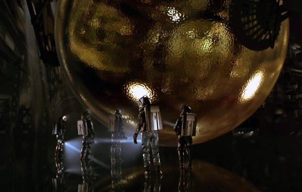People in shiny environment suits looking at the weird gold ripply sphere in the movie SPHERE