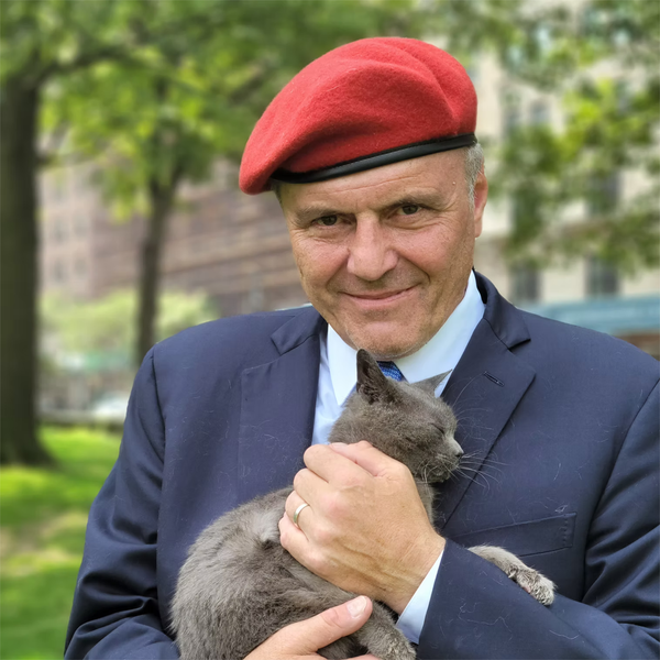 Curtis Sliwa in red beret and blue suit outdoors holding a cat.