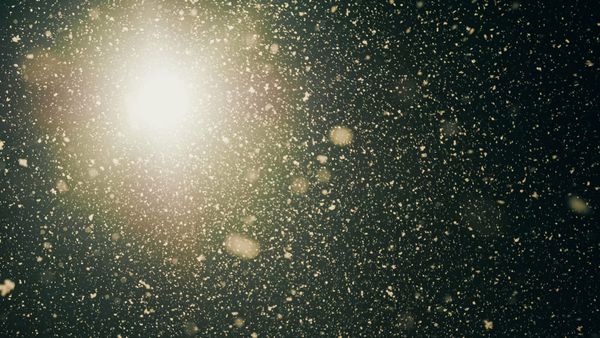 Snowflakes falling seen from below against a bright light at night