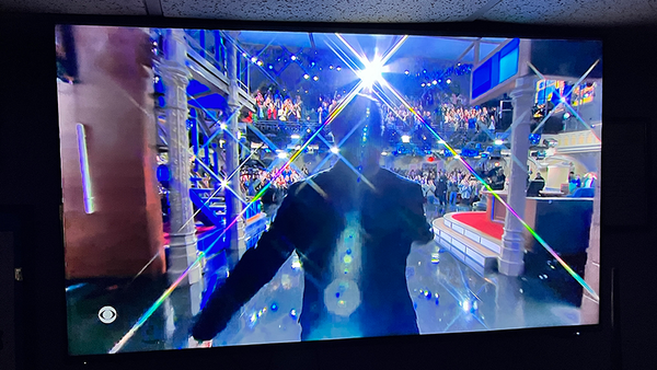 COLBERT VIEWED FROM BEHIND IN SILHOUETTE AS HE WALKS TOWARD THE STAGE AND CHEERING AUDIENCE