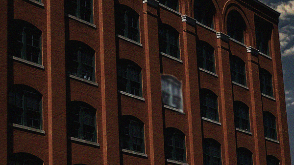 Exterior of a dark building with one window oddly highlighted.