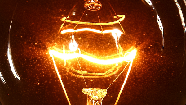 Close view of a lightbulb filament glowing hot in darkness.