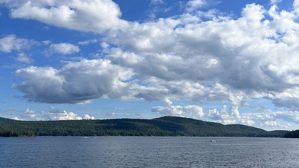 Schroon Lake, the surrounding green-tree countryside, and a blue sky full of puffy clouds